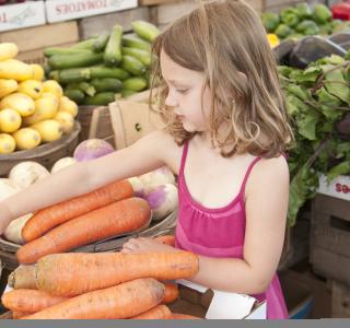 a young girl looking at carrots and other vegetables at a farmers market