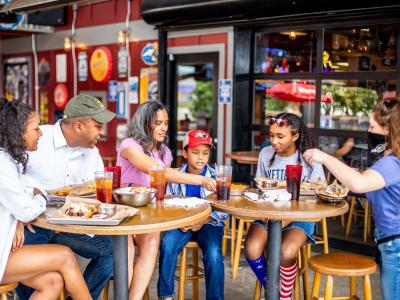 Family and friends gathered around an outdoor restaurant table sharing food and drinks together