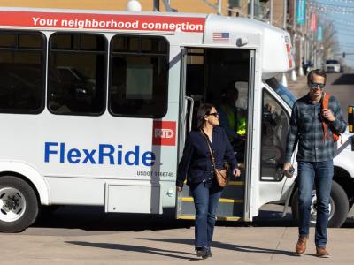 Two people walking off and away from an on-demand, curb-to-curb RTD FlexRide bus.