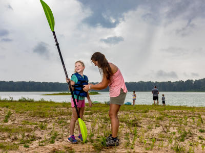 A little girl out of the lake while smiling at her mom at Howell Woods.