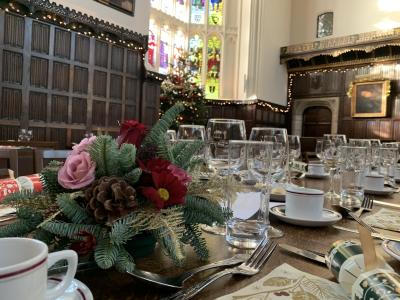 Christ's College Cambridge dining hall set up for a Christmas meal. Glassware, cutlery, crackers & yuletide flowers are in the foreground whilst in the background is dark wood panelling & a stained glass window