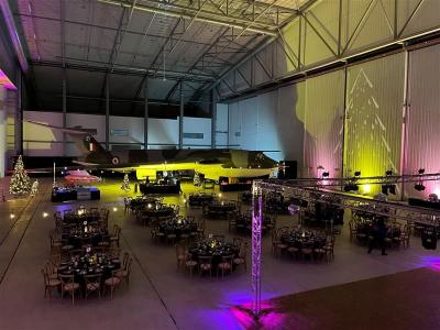 The Conservation Hall at IWM Duxford Cambridge. An airplane is suspended above a series of round tables set up for a Christmas dinner