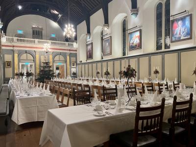Jesus College Hall set up for a formal Christmas dinner. White linens on the tables & a Christmas tree in the background