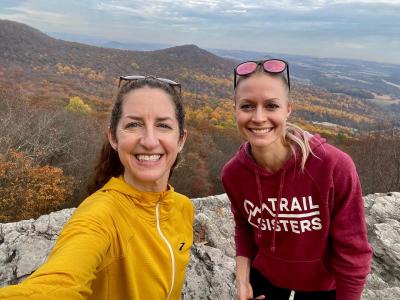 Two people smiling at the top of Hawk Mountain with the last bits of fall foliage in the background.