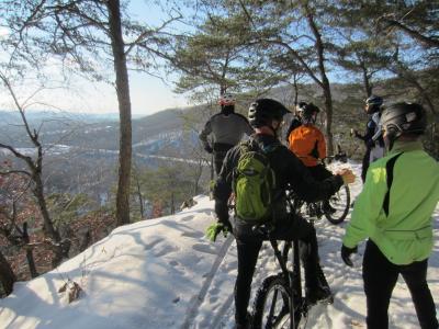 A group of mountain bikers brave the snow to take in the views from a lookout on Neversink Mountain.