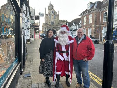 A photo of two people standing on Smith Street in Warwick with Santa Claus standing between them. All threee are smiling at the camera.