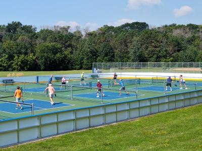 Participants playing pickleball in a multi-use rink during the summertime.