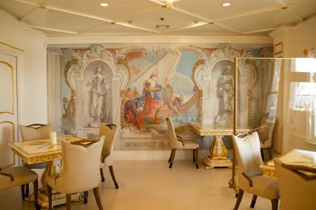 Image of one of Anaheim White House restaurant's dining rooms. The room includes a mirror on the back wall with three tables. The room is white with plenty of gold accents. The dining tables are also white with a gold pattern. The chairs are beige.