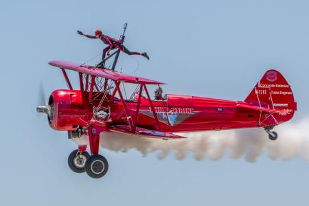 a person wingwalking on a red biplane while it is in flight