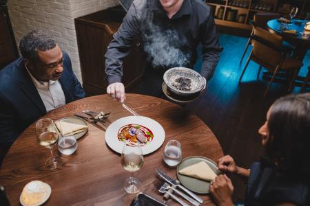 A man and a woman sit at a restaurant table as their waiter serves steak.