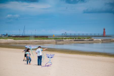 Family of four flying kites on cresent beach with the red lighthouse in the distance