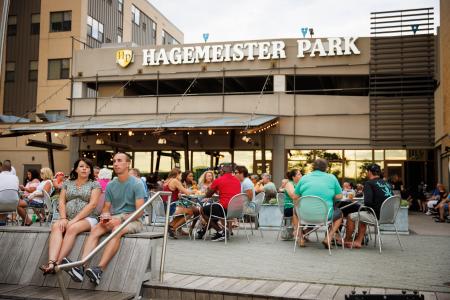 Hagemeister Park Patio filled with people eating and a couple sitting on a bench looking at the Fox River.