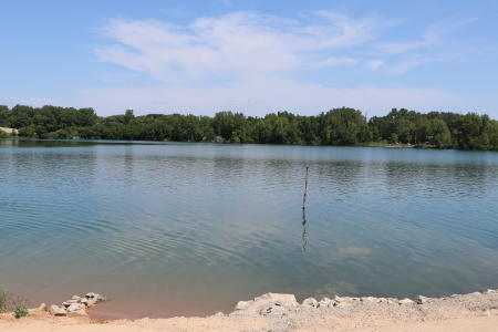 Duck Creek Quarry in the Green Bay area with calm blue water, a small sandy beach in the foreground, and lush green trees lining the shoreline in the background