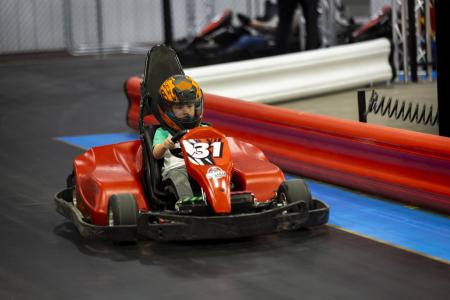 Young boy wearing a helmet and riding a go-kart at Midwest Super Speedway, looking focused as he drives.