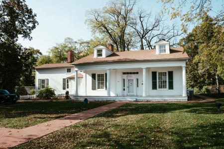 Front Exterior of Hazelwood House in Green Bay, WI. White house with a red roof and red brick walkway.