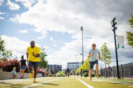 Two men running a 40 yard dash toward the camera. One with shoes on and the other barefoot at Titletown in Green Bay, Wisconsin.