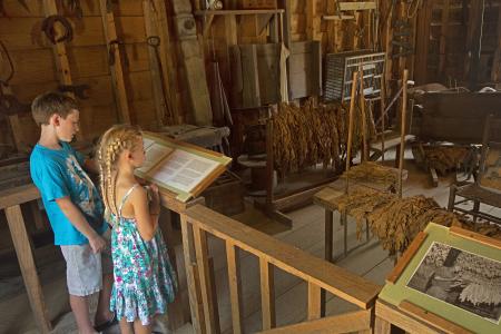 Two children stand at an interactive barn exhibit to read the information on the plaque at the Tobacco Farm Life Museum in Kenly, NC