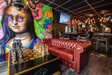 artwork on wall near bar of sugar whiskey sis moonsine bar in covington ky with chess board on coffee table and large red leather couch