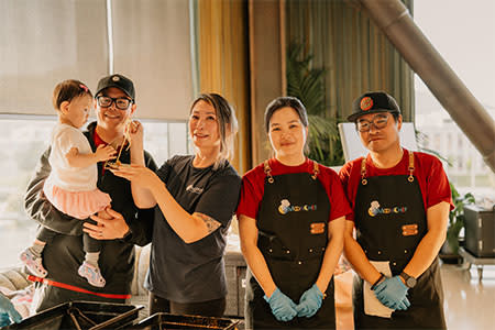 Flavors of the Peninsula participants. Two people wearing aprons, man holding young girl, woman playing with girl.