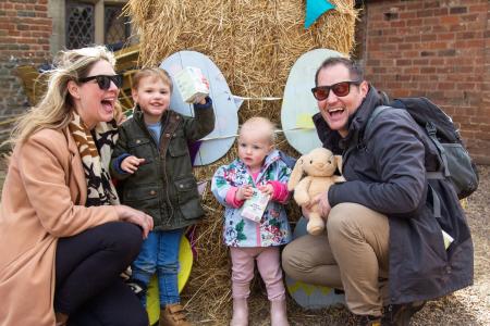 A family of four in front of a hay bale decorated with colourful Easter eggs