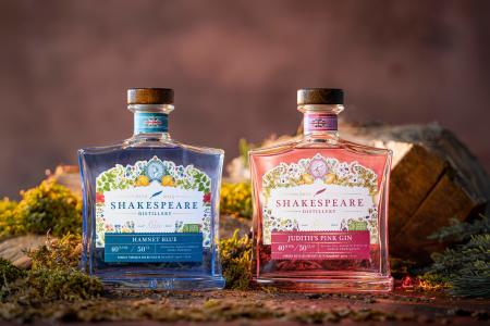 A bottle of Hamnet Blue Gin alongside a bottle of Judith's Pink Gin made by the Shakespeare Distillery sitting on a mossy and flowery forest floor.