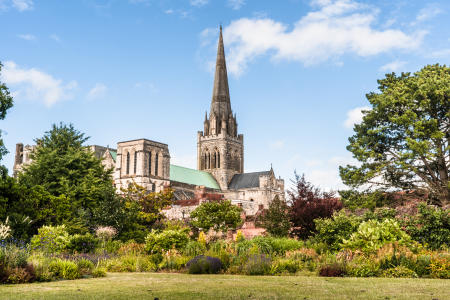 A view of Chichester Cathedral from the gardens with the spire reaching blue sky