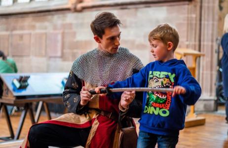 A man in mediaeval costume showing a young boy a sword