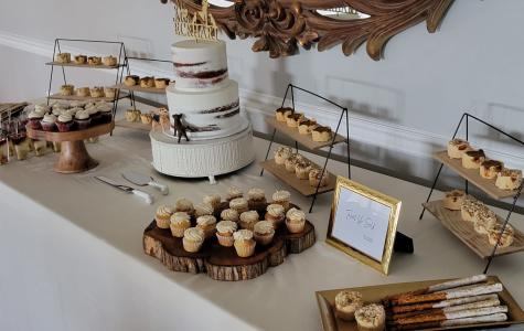 White table with white cupcakes and a 3 tiered white wedding cake with red stripes along the sides