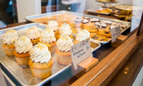 Cupcakes and cookies on metal trays behind the glass at Two Sticks