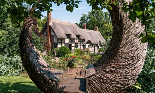 A stunning semi circular shaped willow arch in the foreground of the picture framing Anne Hathaway's Cottage and gardens in the background