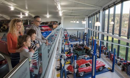 A family overlooking a collection of classic cars from a mezzanine balcony