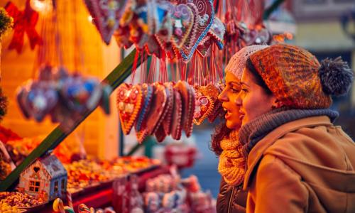 Two shoppers browsing at a Festive Market stall laden with Christmas decorations