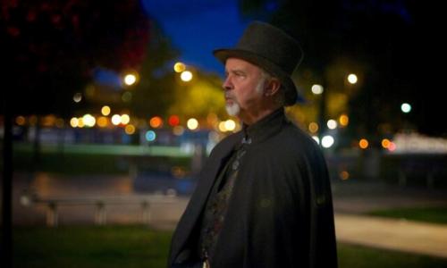 A costumed guide in a cloak and black top hat standing on a moonlight street