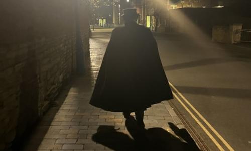 A cloaked figure walking the deserted streets of Stratford by twilight