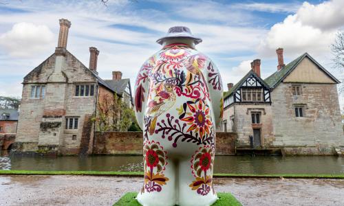 The rear view of a painted snowman statue facing the moat and Baddesley Clinton
