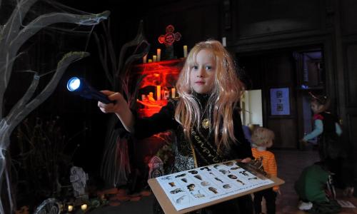 A blond haired girl dressed in a witch costume holding a torch and a quiz in a dark room
