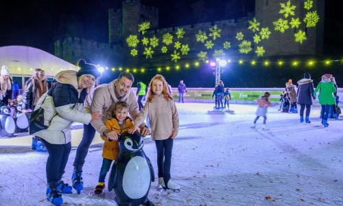 A family ice skating at night on an outdoor ice rink