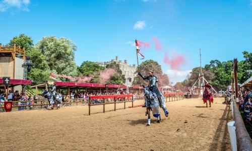 Three actors dressed in costume as mediaeval knights performing on horseback in a live jousting show at Warwick Castle