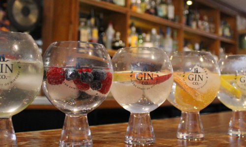 A row of glasses containing different gin and tonics on a wooden bar top