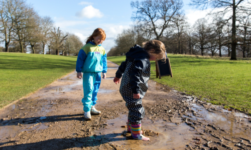 Two girls splashing in a muddy puddle with their wellies on
