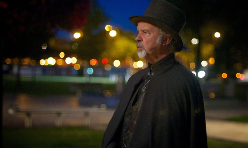 A man stood with a black top hat and cape on looking into the distance