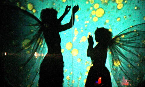 Silhouettes of two figures with fairy wings against a vibrant, whimsical background of glowing yellow and green orbs.