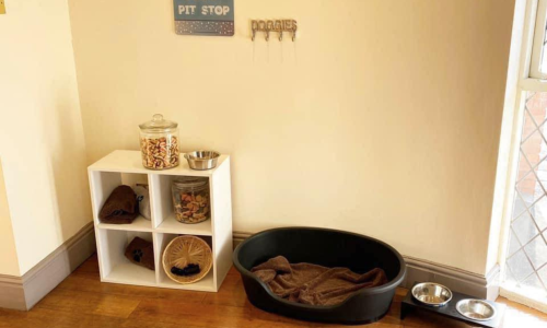 A dog basket with dog bowls and biscuits beneath a sign reading Doggy Pit Stop