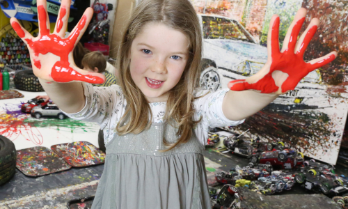 A girl holding both her hands up with are covered in red paint