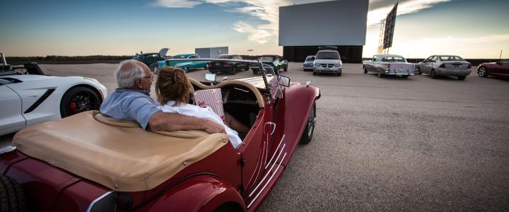 A couple sits in a vintage car in front of a movie screen at Stars & Stripes Drive-In Theater