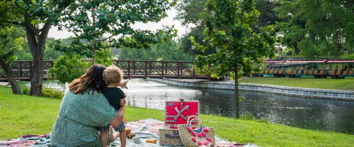 A mom and child have a picnic by the water at Landa Park.