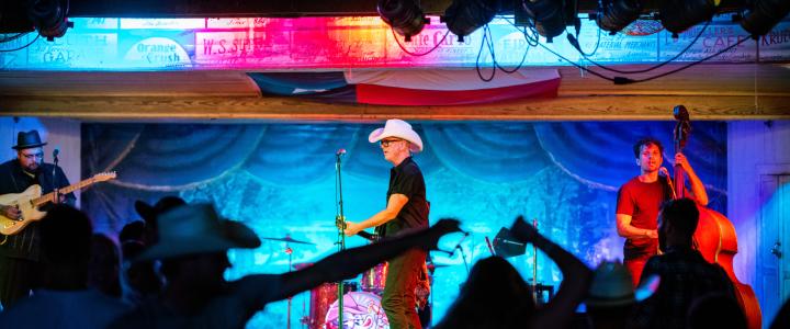 A couple dances in the foreground of a Two Tons of Steel show at Gruene Hall