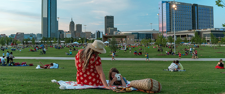 Small groups of people laying on blankets and parks at Scissortail Park 