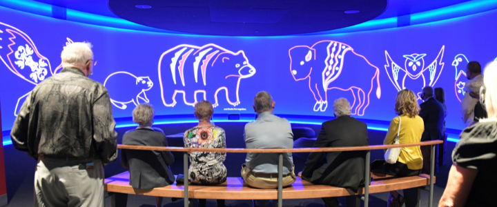 Individuals enjoying a multimedia exhibit inside of the First Americans Museum