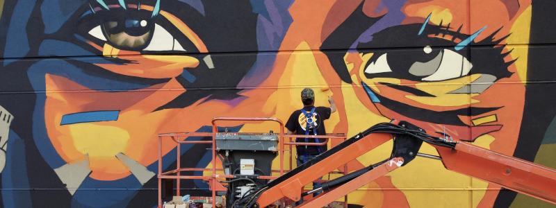 Image of artist on lift painting a mural of an African-American child's eyes.